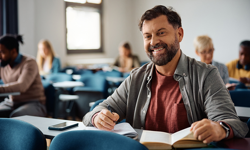 Happy mature student taking learning during a class in lecture hall 